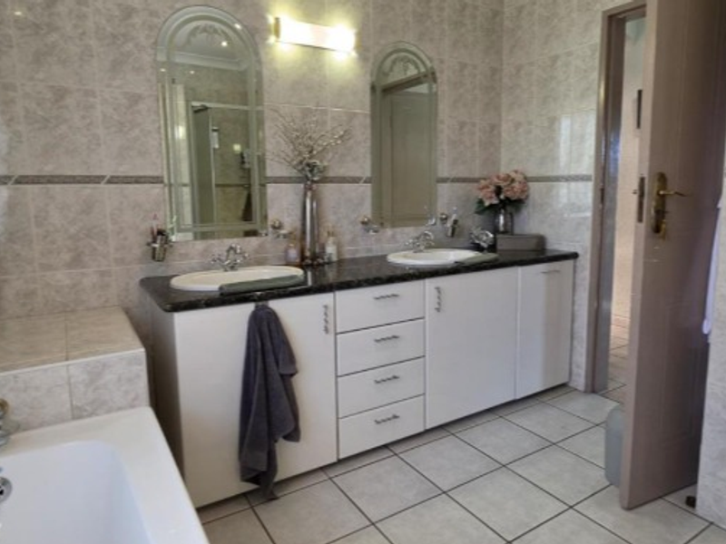 A functional bathroom featuring a double vanity with built-in cabinetry, tiled walls and flooring, and a built-in bathtub.