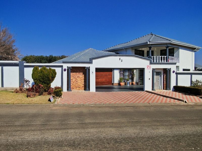 Front elevation of a residential property featuring a tiled roof, brick-paved driveway, perimeter wall, and a balcony with decorative pillars.