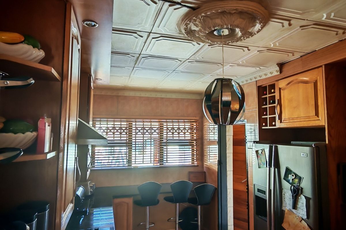 A kitchen featuring wooden cabinetry, a built-in wine rack, and decorative ceiling tiles with a central ceiling rose and pendant lighting.