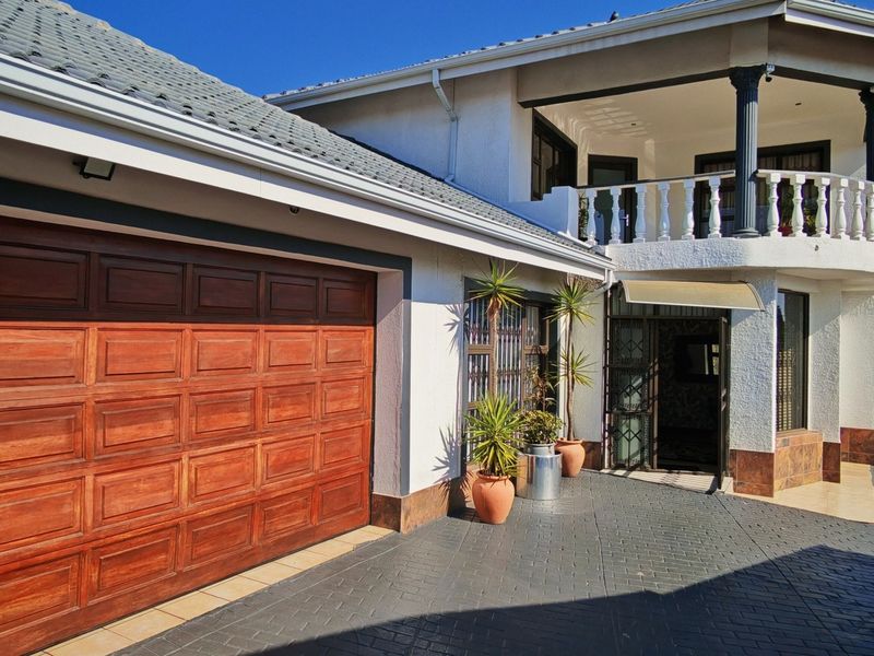 Front elevation of a residential property featuring a wooden double garage door, paved driveway, and an upper-level balcony with decorative balustrades.