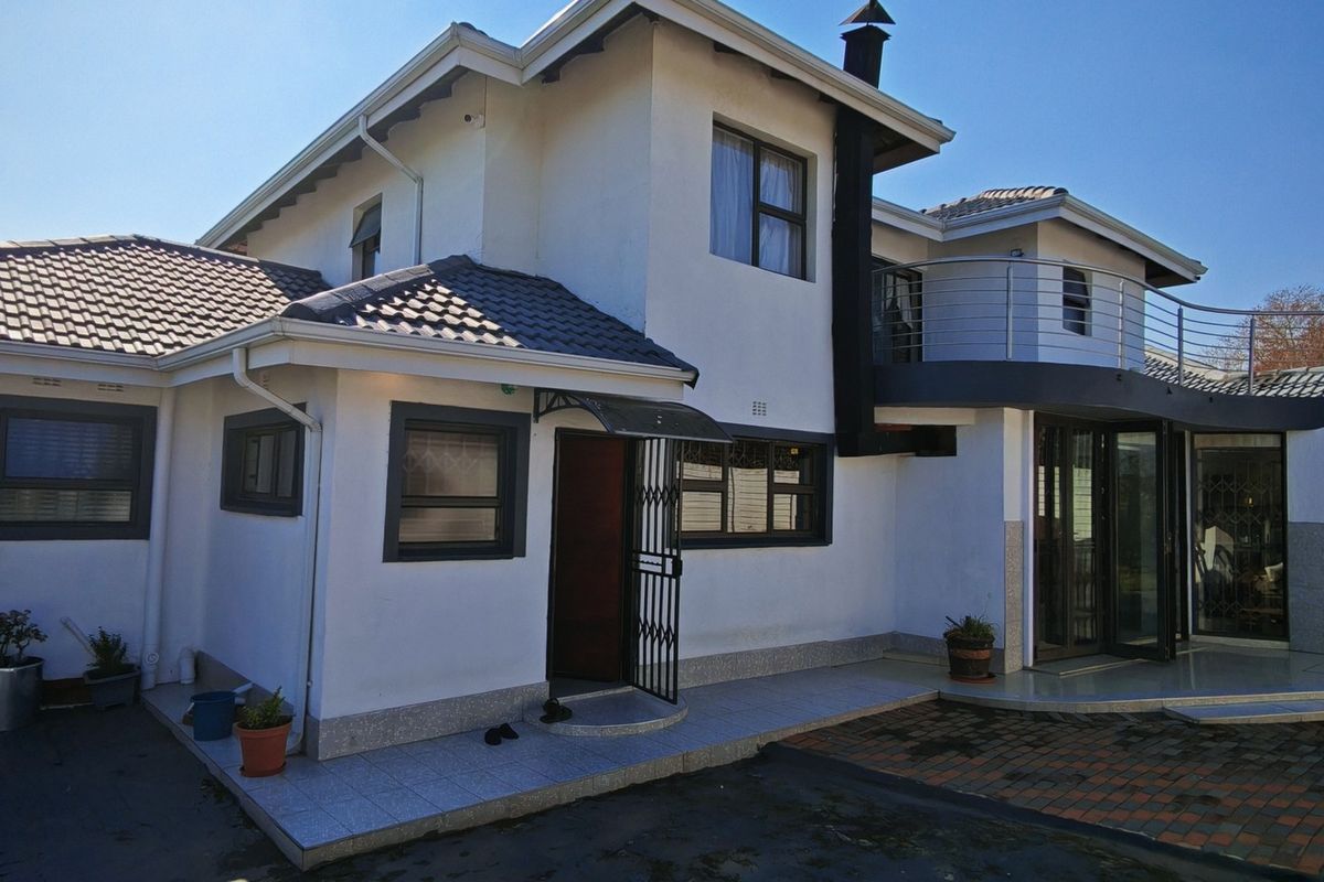 Rear elevation of a two-story house featuring a tiled roof, balcony, external chimney, and paved patio area with sliding door access.
