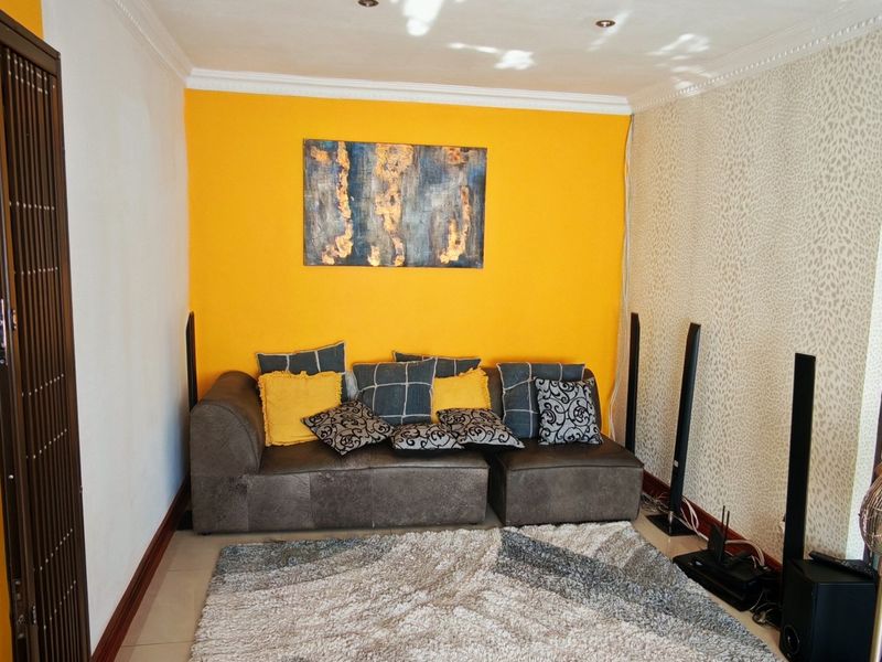 A living room featuring tiled flooring, recessed downlighting, and decorative cornice detailing, with a distinct yellow accent wall.
