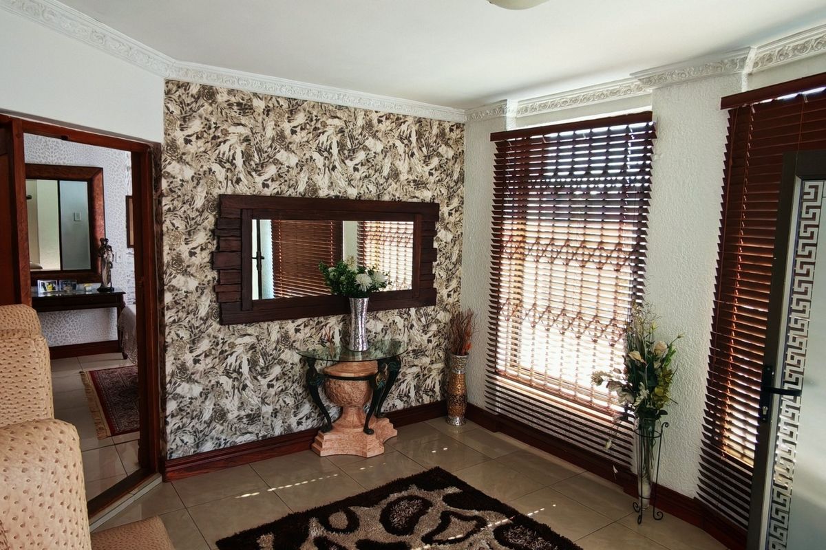 A living area featuring tiled flooring, crown molding, and textured wallpaper, with wooden venetian blinds providing natural light control.