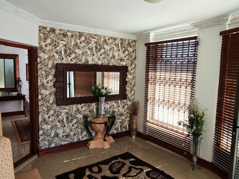 A living area featuring tiled flooring, crown molding, and textured wallpaper, with wooden venetian blinds providing natural light control.