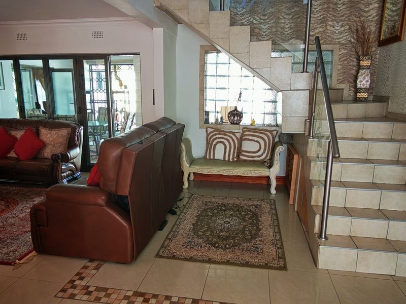 Spacious living area featuring a tiled staircase with a modern glass balustrade, glass block feature window, and sliding doors leading to the patio.