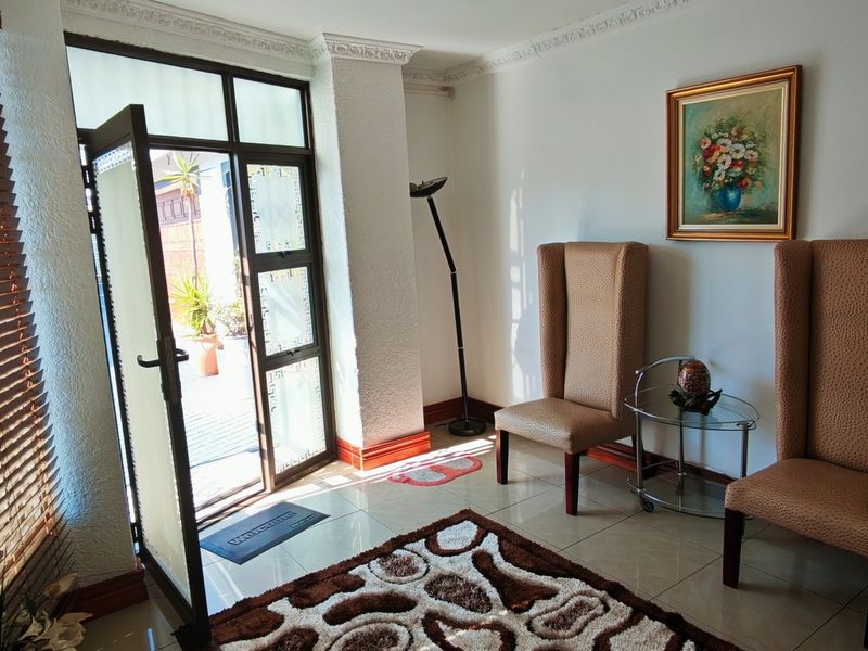 A bright and welcoming entrance hall featuring tiled flooring, decorative ceiling cornicing, and a glass-panelled door providing natural light and access to the exterior.