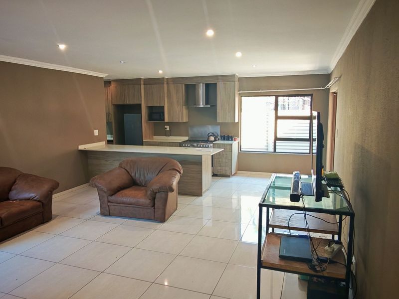 Open-plan living area featuring tiled floors, recessed lighting, and a modern kitchen with a breakfast island, built-in oven, and extractor fan.
