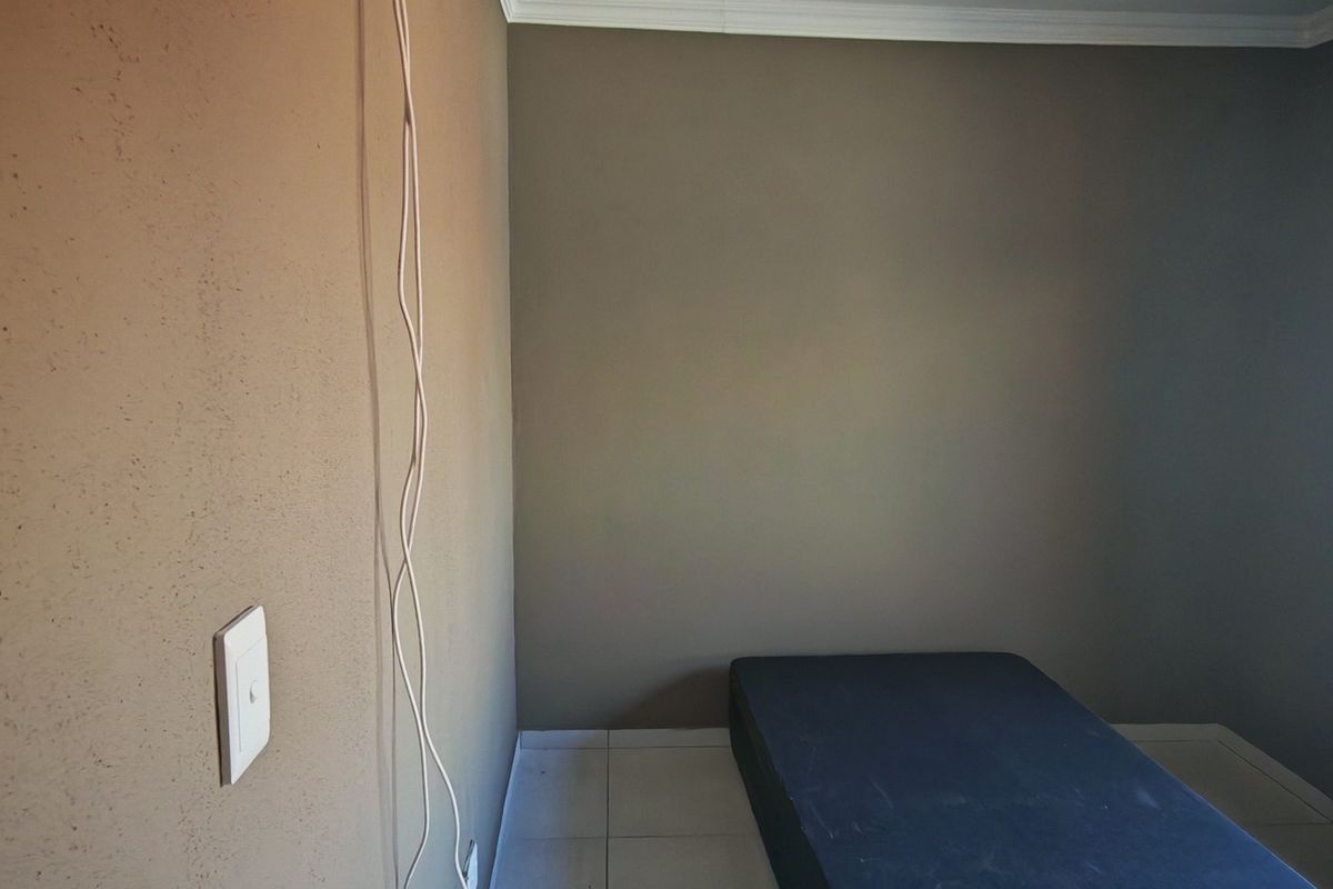 A compact bedroom featuring tiled flooring, a curtain rail, and neutral wall finishes, currently presented as an empty space.