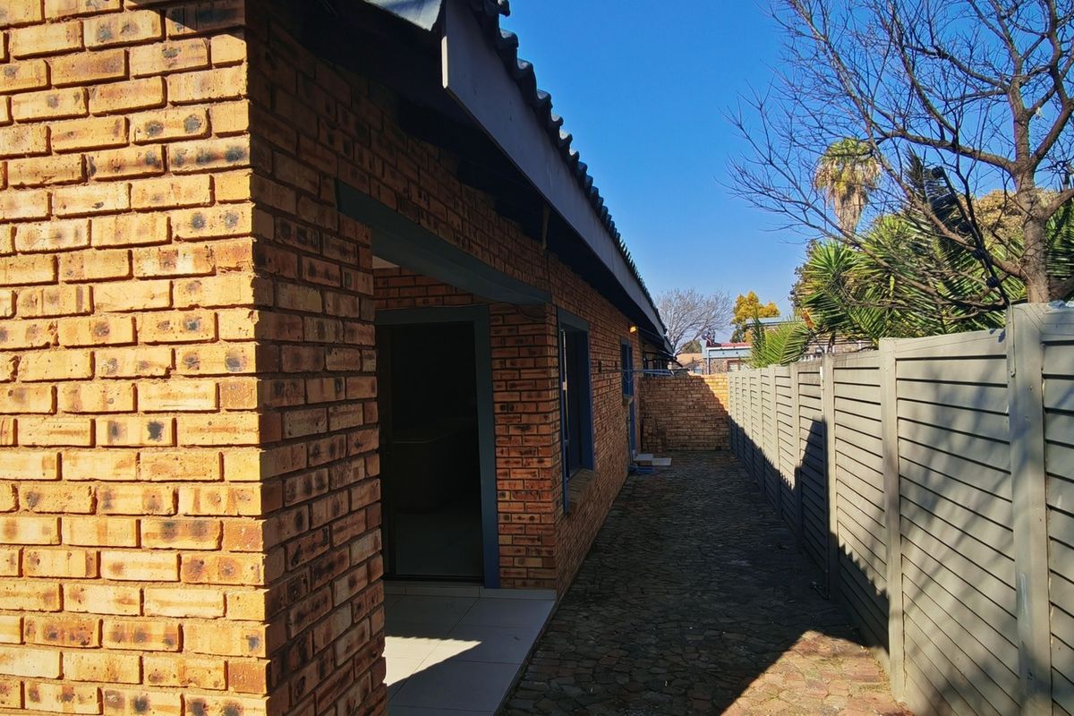 A side view of the property featuring a face brick exterior, a paved walkway, and a perimeter fence.