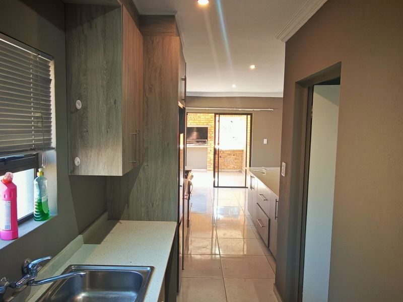 Modern kitchen featuring sleek wood-finish cabinetry, stone countertops, and tiled flooring, leading through to an open-plan living area and outdoor patio space.
