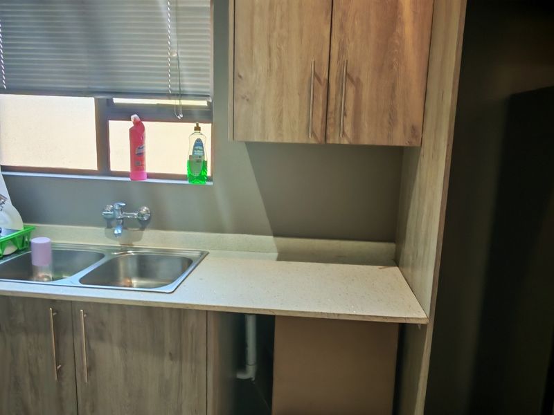 A functional kitchen area featuring laminate cabinetry, a double stainless steel sink with a mixer tap, and a stone-look countertop.
