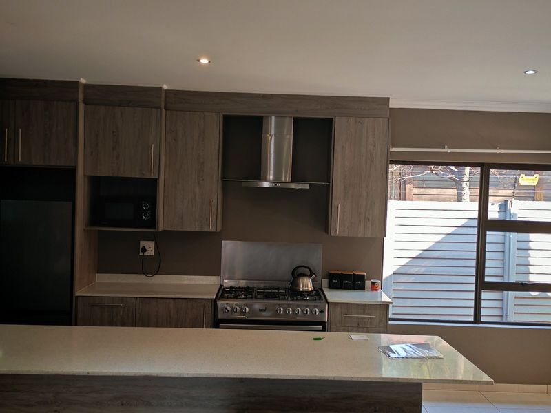 Modern kitchen featuring wood-finish cabinetry, stone countertops, a gas stove with extractor fan, and a breakfast nook overlooking the exterior.