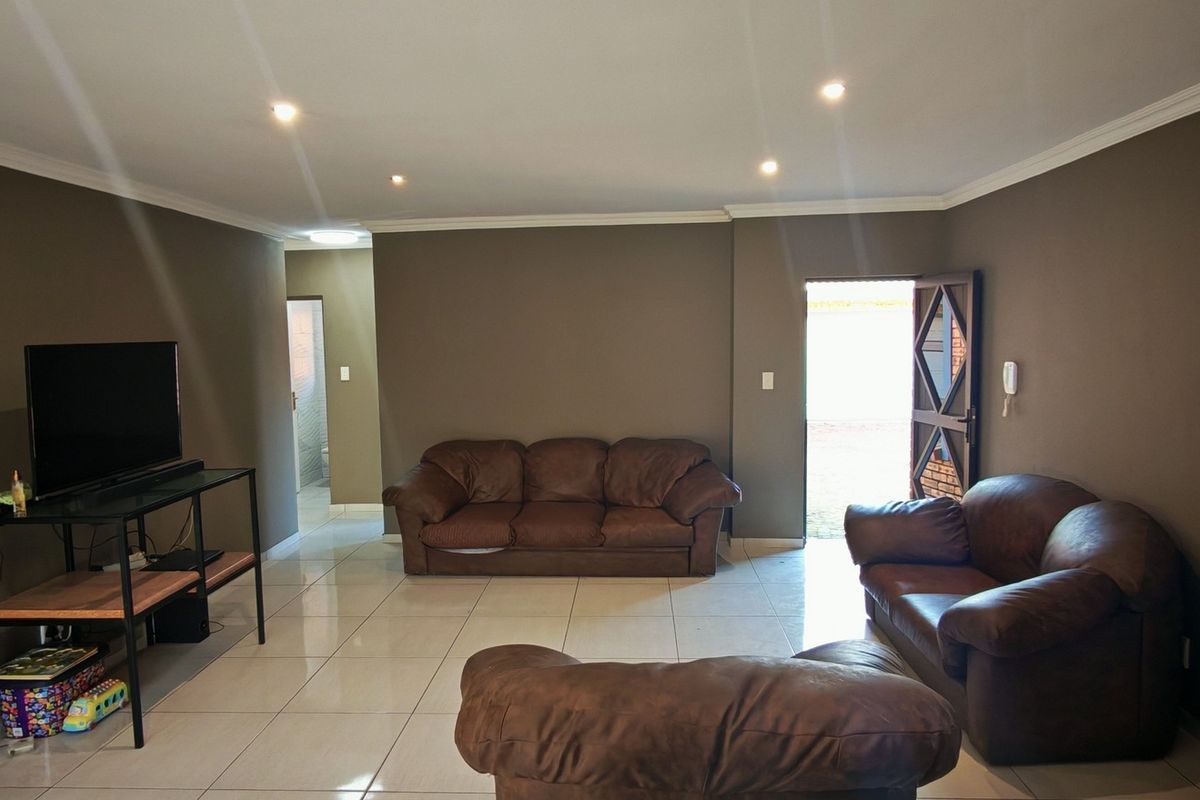 A spacious living room featuring neutral wall tones, tiled flooring, recessed downlighting, and crown molding, providing a functional and well-lit living space.