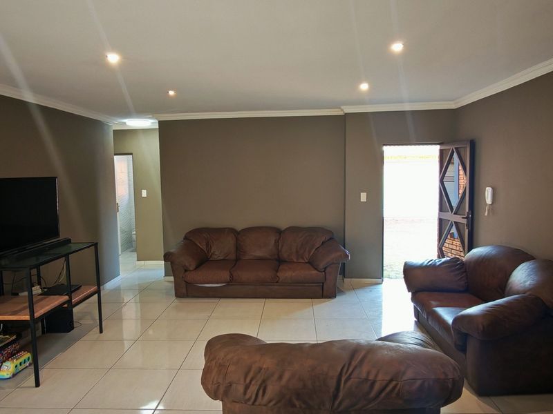 A spacious living room featuring neutral wall tones, tiled flooring, recessed downlighting, and crown molding, providing a functional and well-lit living space.