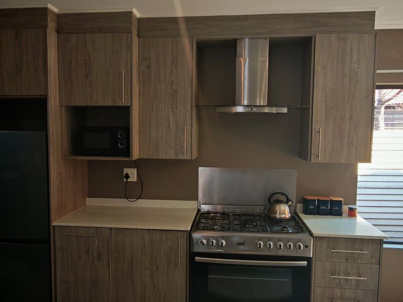 Modern kitchen featuring wood-grain cabinetry, stone countertops, a stainless steel gas stove with extractor fan, and a built-in microwave.