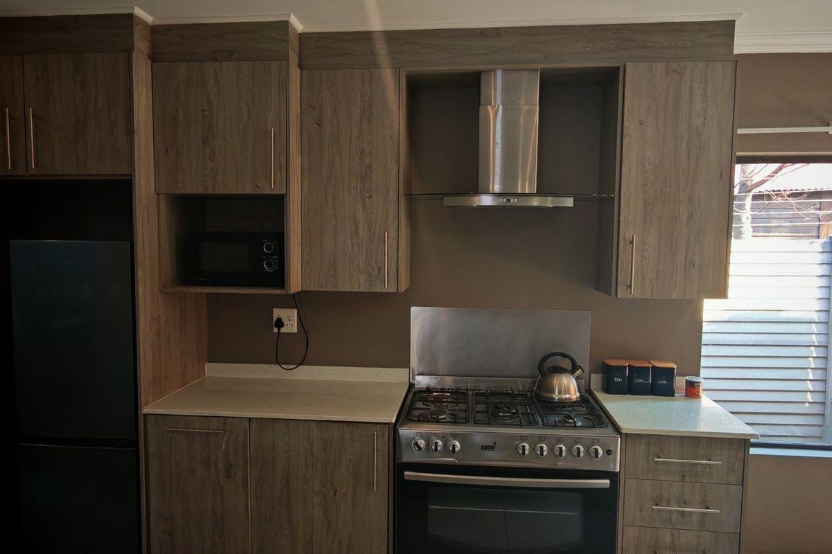 Modern kitchen featuring wood-grain cabinetry, stone countertops, a stainless steel gas stove with extractor fan, and a built-in microwave.