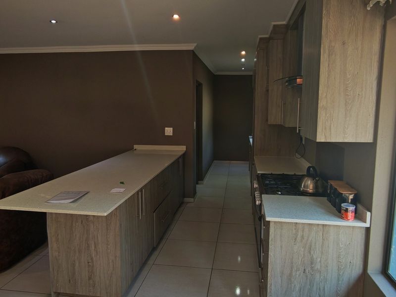 Open-plan kitchen featuring modern wood-finish cabinetry, stone countertops, gas hob, and direct access to the outdoor area through a sliding glass door.