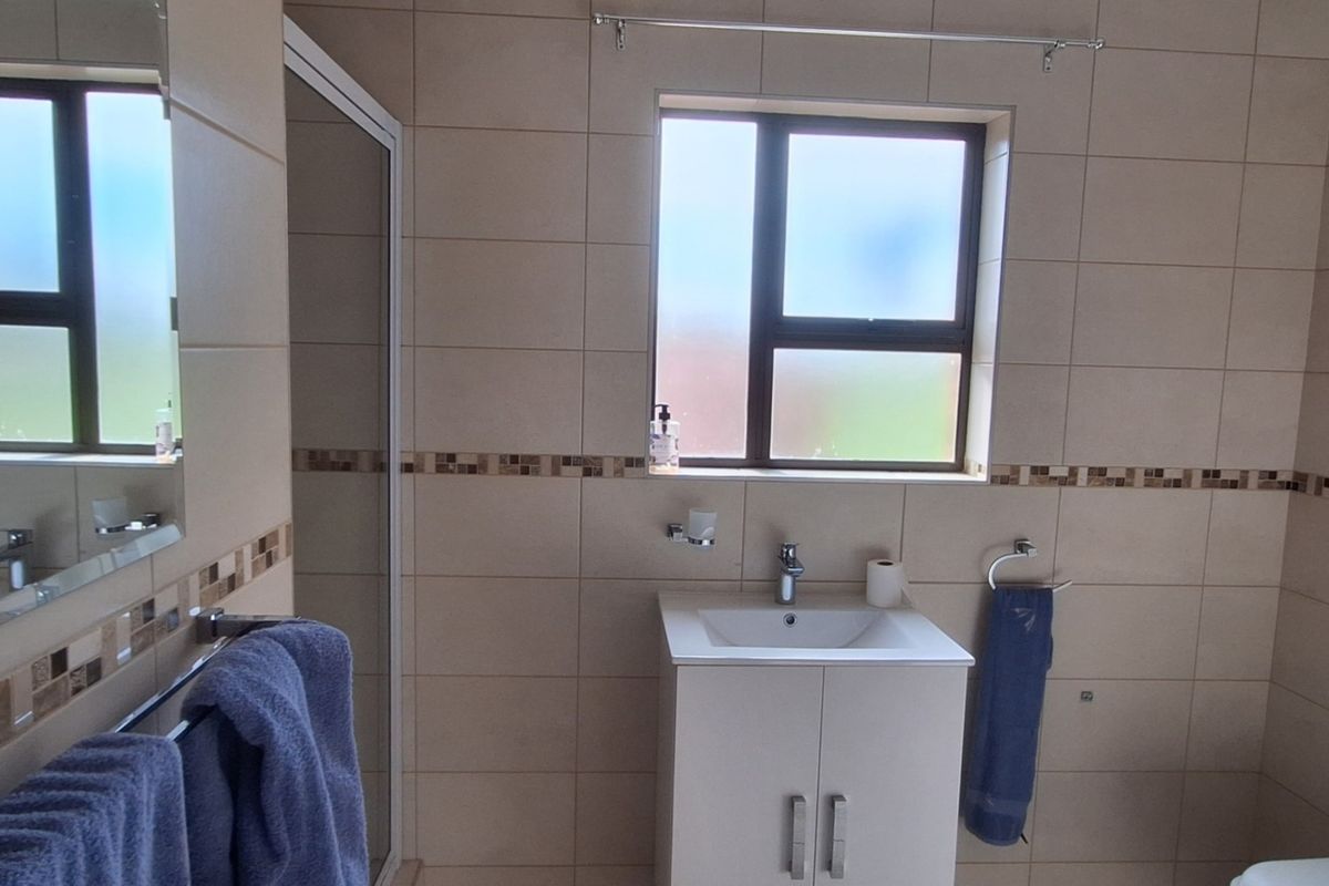 A functional bathroom featuring a vanity cabinet with basin, a shower enclosure, and neutral wall tiling with a decorative mosaic border.