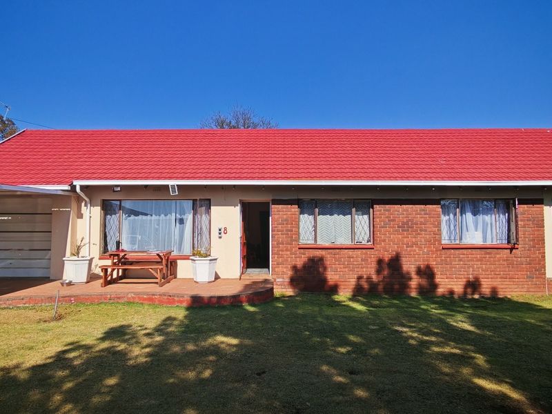 Front view of a single-story brick house featuring a prominent red tiled roof, attached garage, and a spacious front lawn.