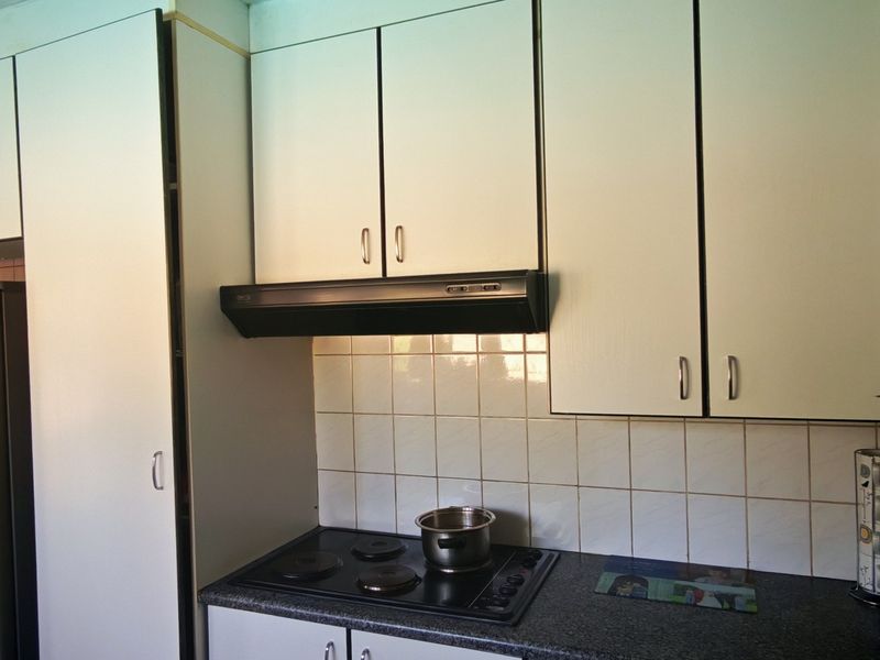 A functional kitchen featuring white built-in cabinetry, a tiled backsplash, and an integrated electric hob with an extractor fan.