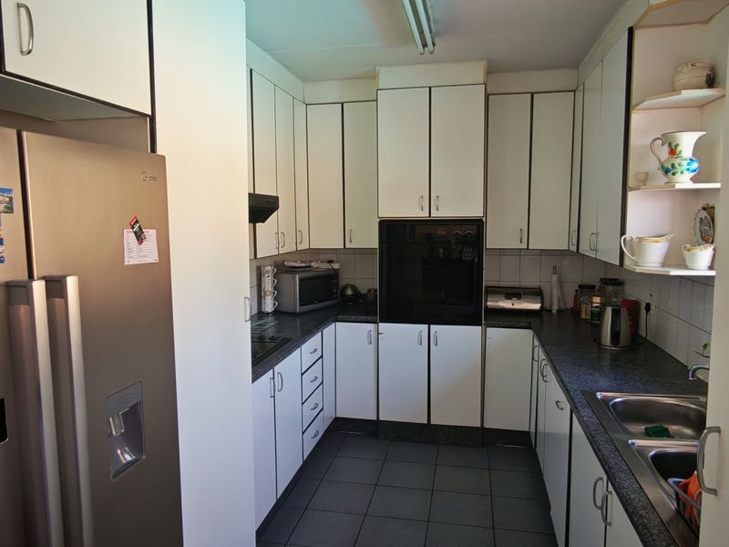 A functional galley-style kitchen featuring white cabinetry, dark laminate countertops, integrated oven, and a double bowl stainless steel sink.