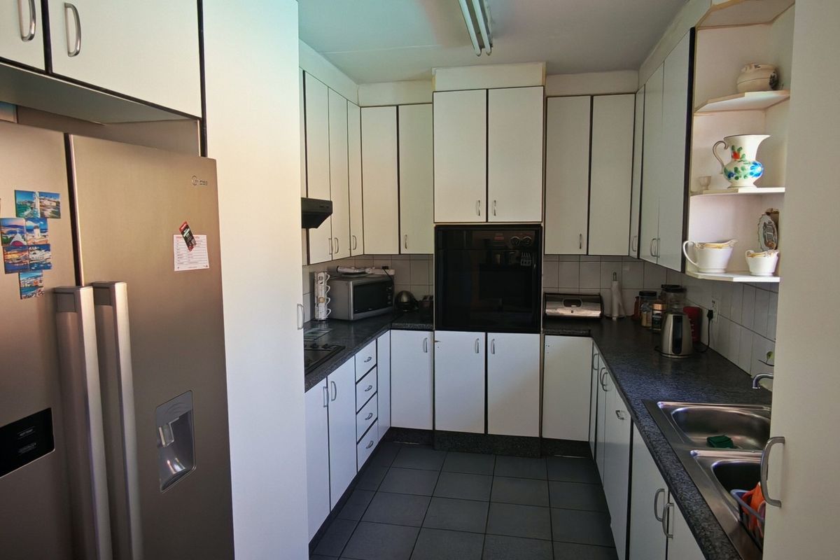 A functional galley-style kitchen featuring white cabinetry, dark laminate countertops, integrated oven, and a double bowl stainless steel sink.