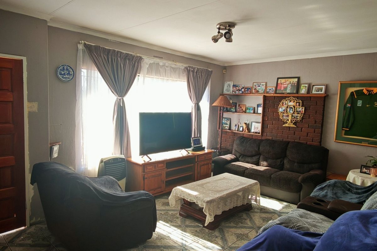 A living room featuring a brick accent wall, tiled flooring, and natural light from a large window.