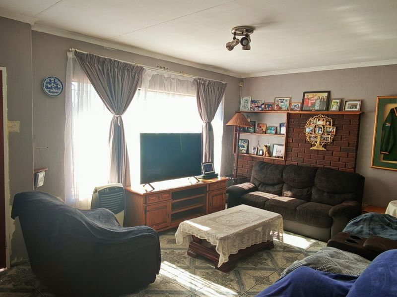 A living room featuring a brick accent wall, tiled flooring, and natural light from a large window.