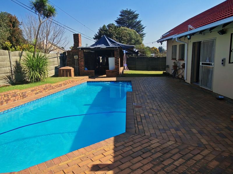 Outdoor pool area featuring a swimming pool, brick paved patio, and a built-in braai structure, set within a private garden with boundary walls.