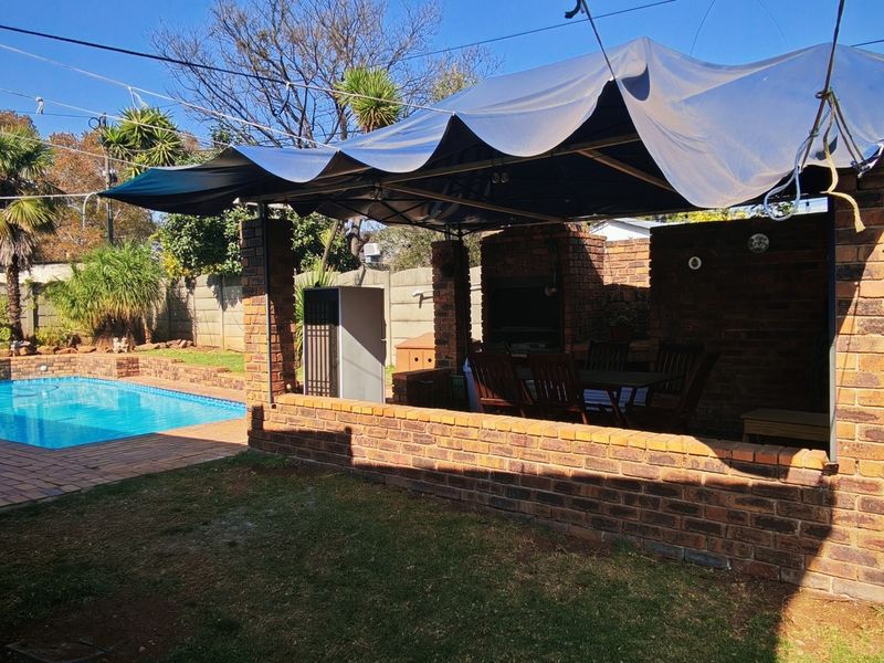 Outdoor entertainment area featuring a swimming pool, paved surround, and a brick-built braai structure with a temporary fabric canopy.