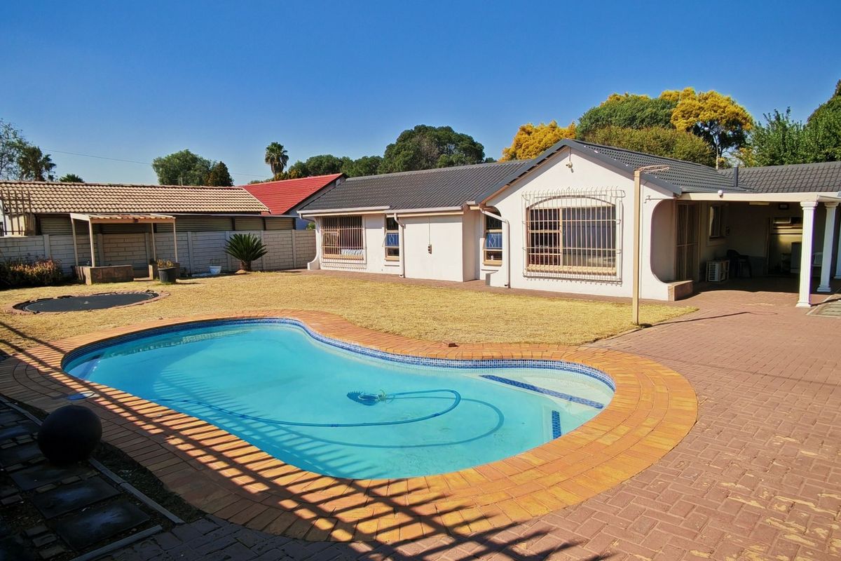 Rear view of the property featuring a swimming pool, paved patio area, and a well-maintained garden with boundary walling.