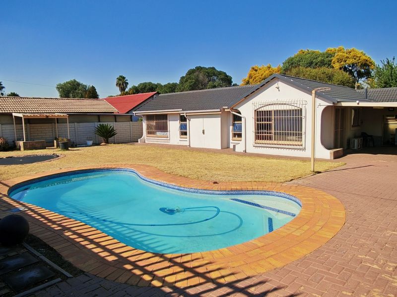 Rear view of the property featuring a swimming pool, paved patio area, and a well-maintained garden with boundary walling.