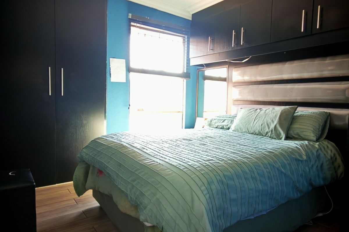A bedroom featuring dark built-in cupboards, overhead storage units, and laminate flooring, providing functional storage space.