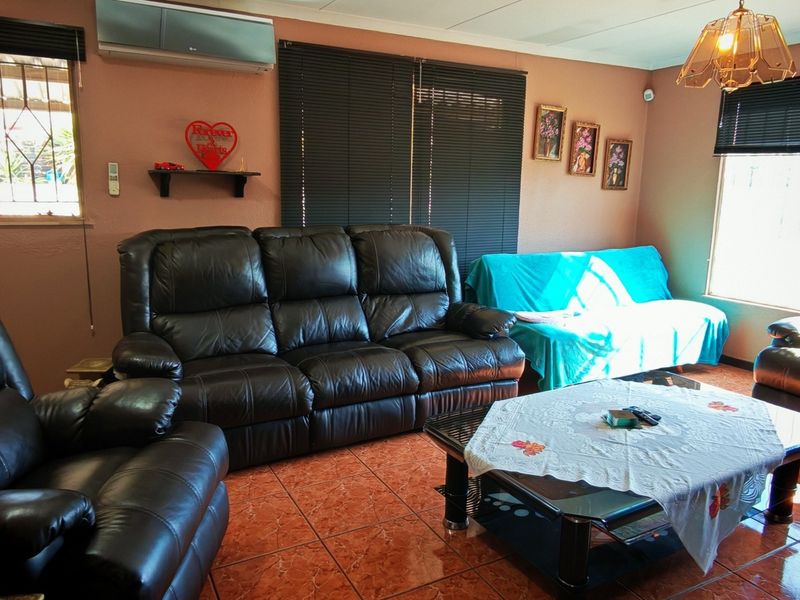 A living room featuring tiled flooring, air conditioning, and security bars on the windows, providing a functional and lived-in space.