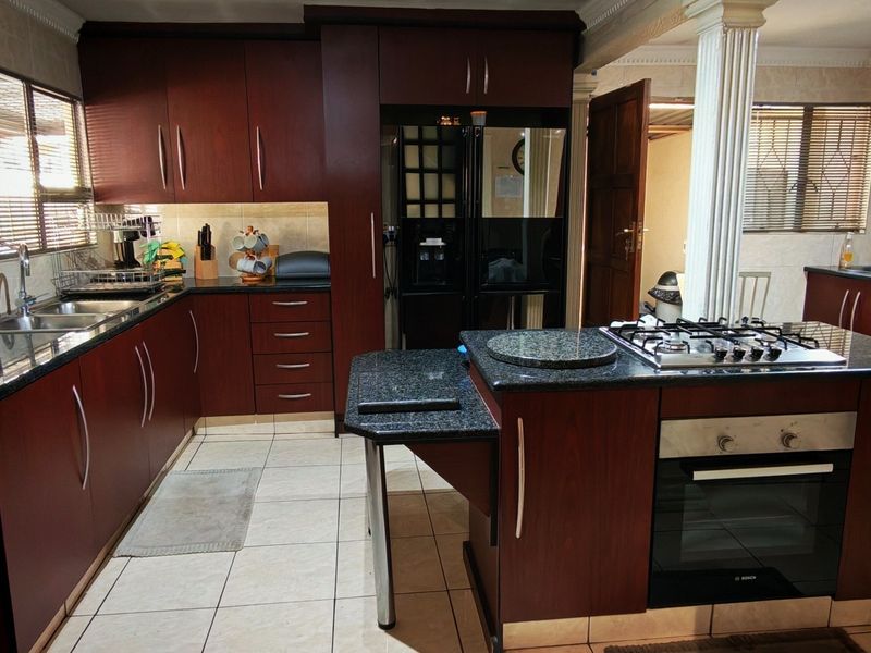 A functional kitchen featuring dark wood cabinetry, granite countertops, a central island with a gas hob and built-in oven, and tiled flooring.