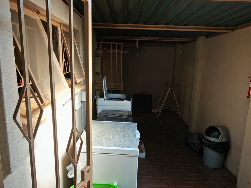 A functional laundry area featuring paved flooring, a corrugated metal roof, and secure metal gate access.
