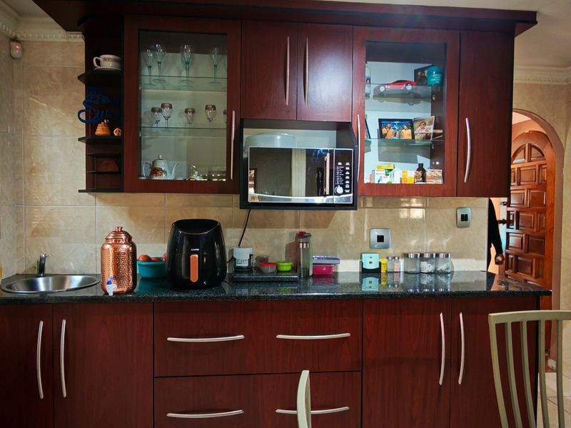 A functional kitchen featuring dark wood cabinetry, granite countertops, a built-in microwave, and tiled wall finishes with natural light from window blinds.