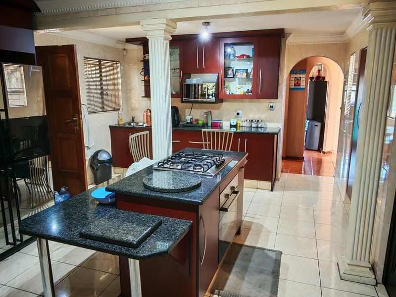 A spacious kitchen featuring dark wood cabinetry, granite countertops, a central island with a gas hob, and decorative columns leading to an adjacent area.