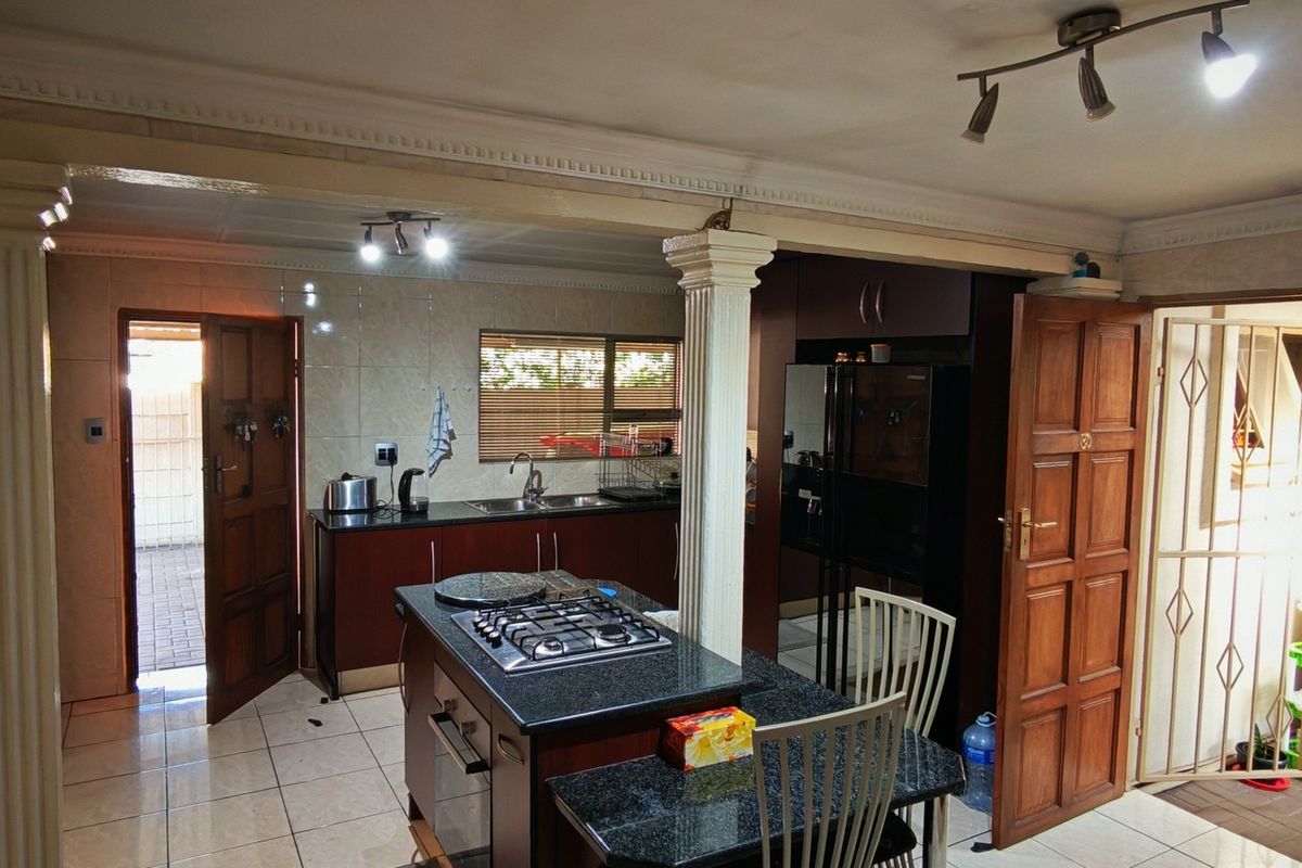 Spacious kitchen featuring dark cabinetry, granite countertops, a central island with a gas hob, and direct access to the exterior.