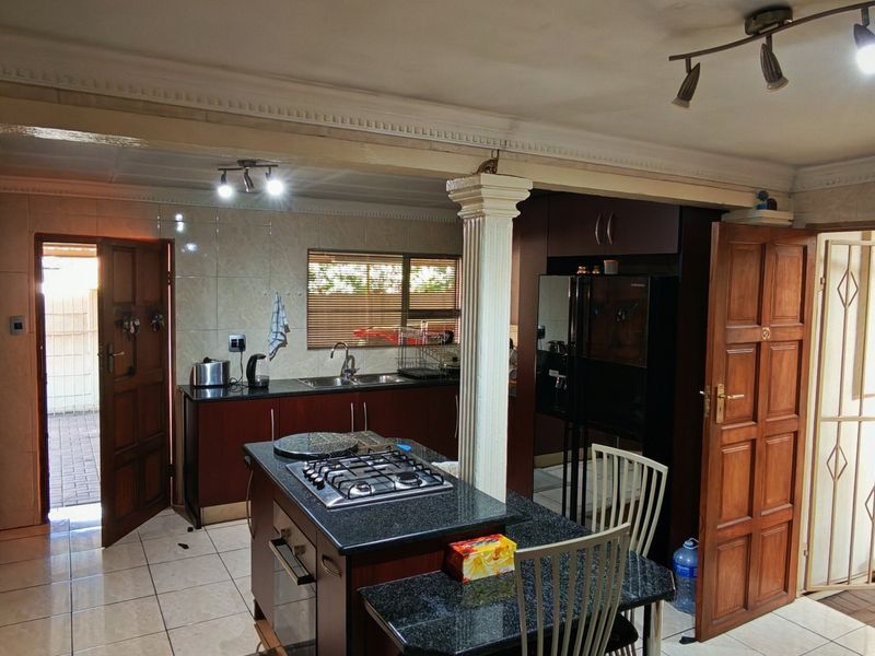 Spacious kitchen featuring dark cabinetry, granite countertops, a central island with a gas hob, and direct access to the exterior.