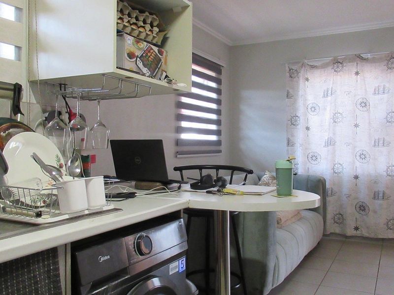Compact open-plan living area featuring a functional kitchenette with built-in cabinetry, integrated washing machine, and tiled flooring.