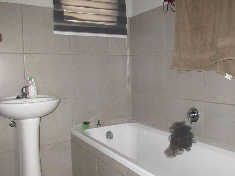 A functional bathroom featuring a pedestal basin, bathtub with mixer tap, and neutral wall tiling.