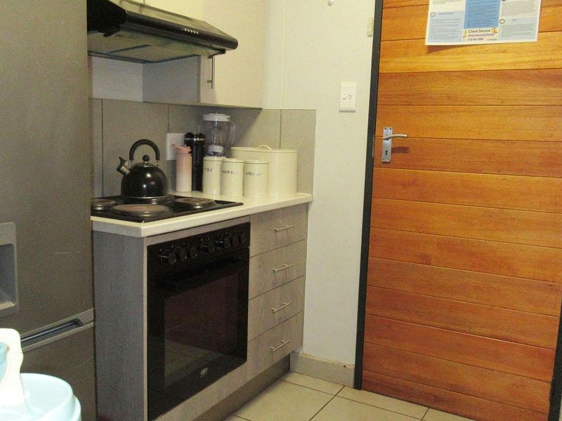 Compact kitchen area featuring a built-in oven, electric hob, extractor fan, and tiled splashback, finished with a wooden door.
