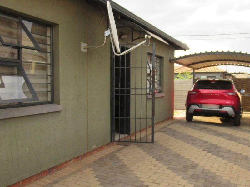 Exterior view of the property featuring a paved driveway, a covered carport, and a secure entrance with a metal security gate.