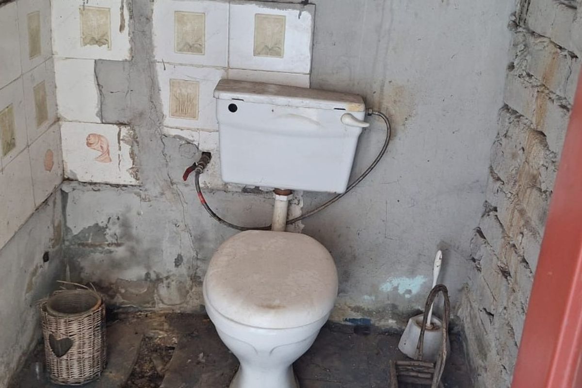 A small, unfinished bathroom featuring a standard toilet, exposed brickwork, and damaged wall plaster requiring significant renovation and repair.