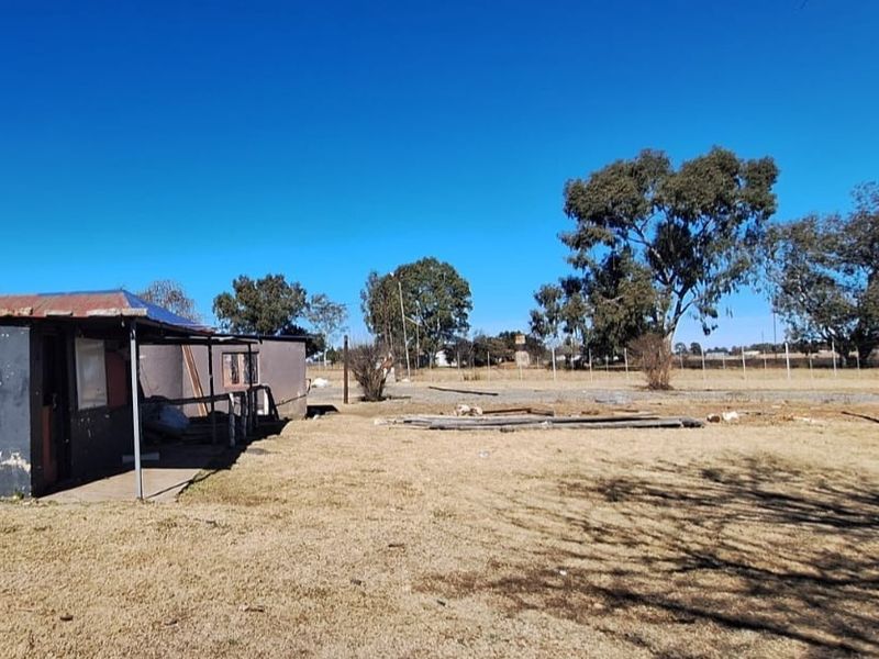 A view of the rear exterior of a small holding property featuring a weathered structure with a corrugated metal roof and expansive open land.