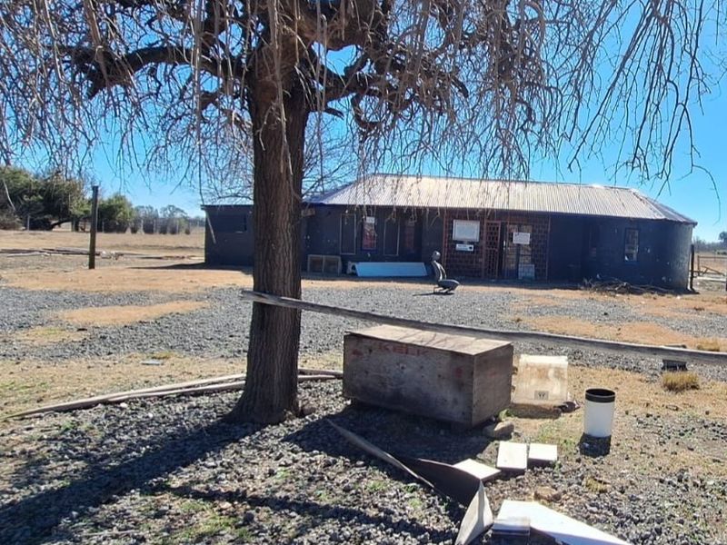 Exterior view of a small holding property featuring a single-story structure with a corrugated metal roof and gravel grounds.