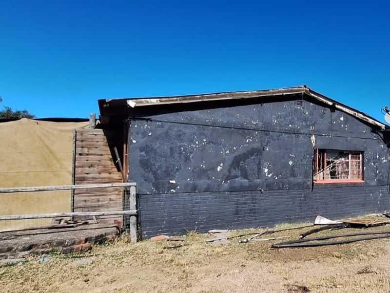 Rear view of a small holding structure showing significant exterior wear, peeling paint, and damaged building elements requiring maintenance.