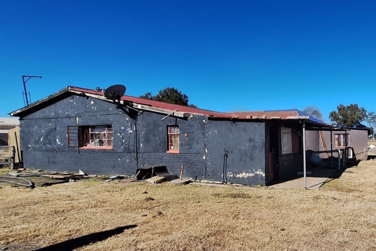 Rear view of a small holding dwelling showing significant exterior wear, peeling paint, and structural deterioration requiring maintenance and renovation.