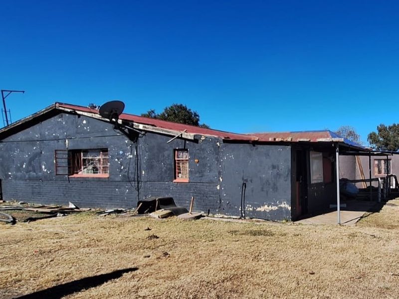 Rear view of a small holding dwelling showing significant exterior wear, peeling paint, and structural deterioration requiring maintenance and renovation.